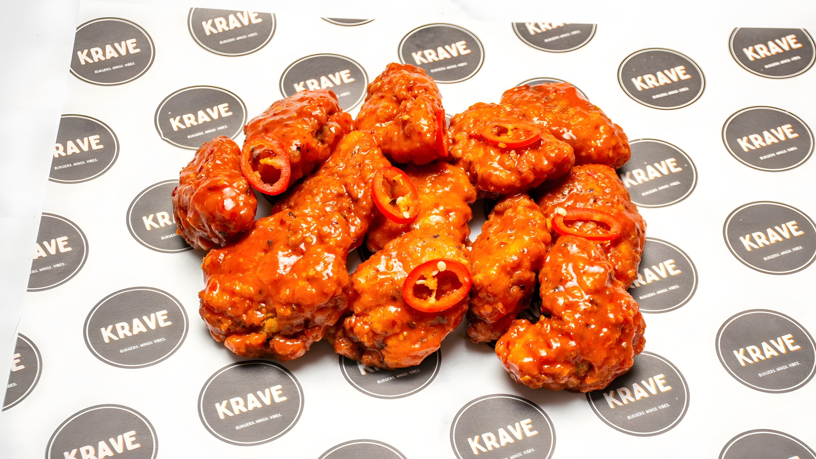 A pile of KRAVE buffalo wings glazed in hot sauce with fresh red chilli